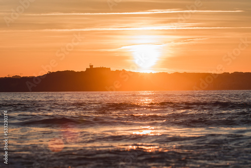 Spectacular panoramic view of a castle on the horizon on the mountain over the sea at sunset during a surf and travel week experience in Somo, Cantabria (Spain)