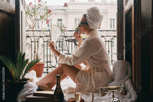 Beautiful young woman in bathrobe doing make-up while sitting between the room and balcony photo