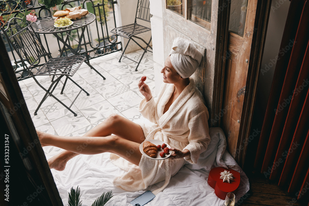 Top view of happy young woman in bathrobe enjoying food while relaxing on the hotel balcony