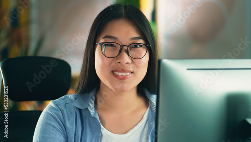 Asian woman in glasses looking at screen of computer while working on 3D modeling project or design remotely from home or surfing the internet in spare time. Freelance