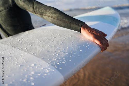 Unknown woman wearing black wetsuit holding white surfboard while standing