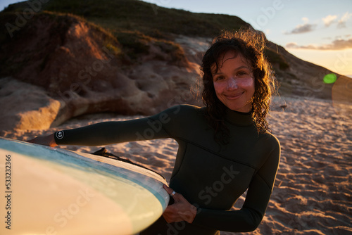 Surfer woman with wet hair holding surfboard on summer beach while enjoying her sport holidays