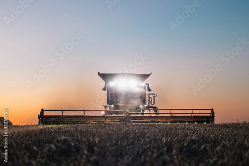 Front view of combine harvester working in a field at dusk with headlights turned on © uslatar