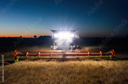 Obraz na płótnie Working combine harvester captured in motion with front headlights illuminating the field at night w salonie