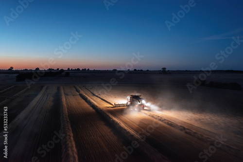 Panoramic aerial landscape view of working combine harvester at night with lights illuminating the field photo