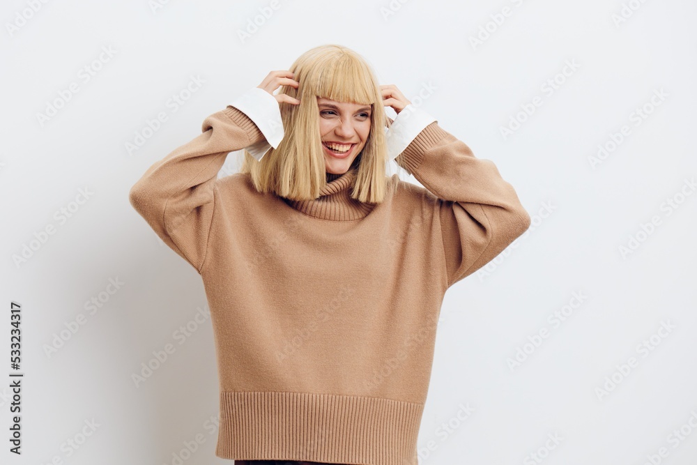 Horizontal photo, a woman on a white background in a beige sweater with beautiful blond hair and a smile with her hands near her face is having fun Horizontal photo, a woman on a white background in a beige sweater with beautiful blond hair and a smile with her hands near her face is having fun