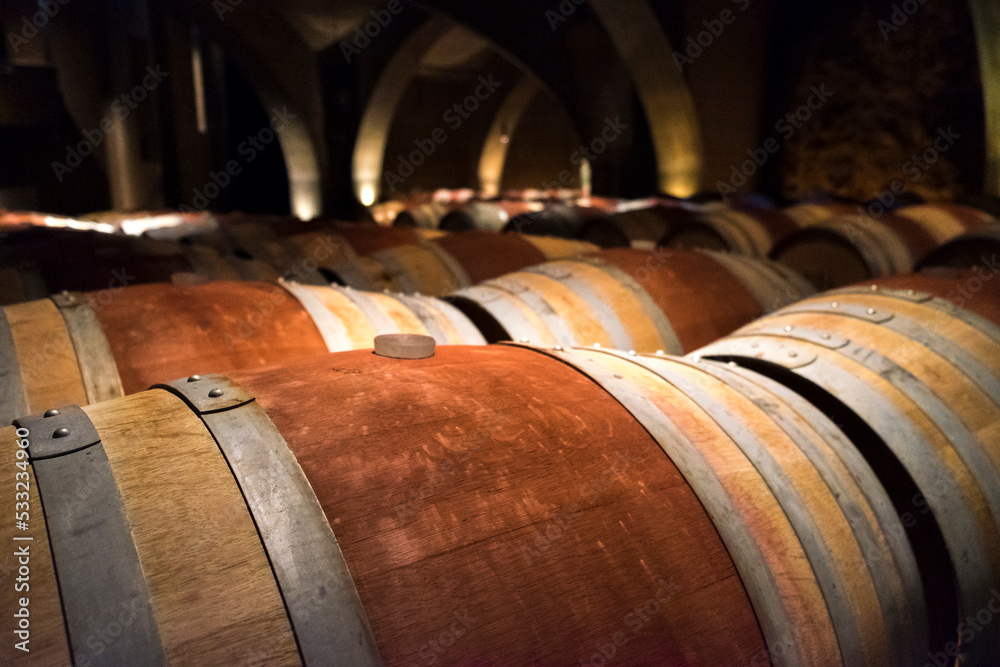Wood wine barrels with reddish brown stripes in a dark wine cellar.
