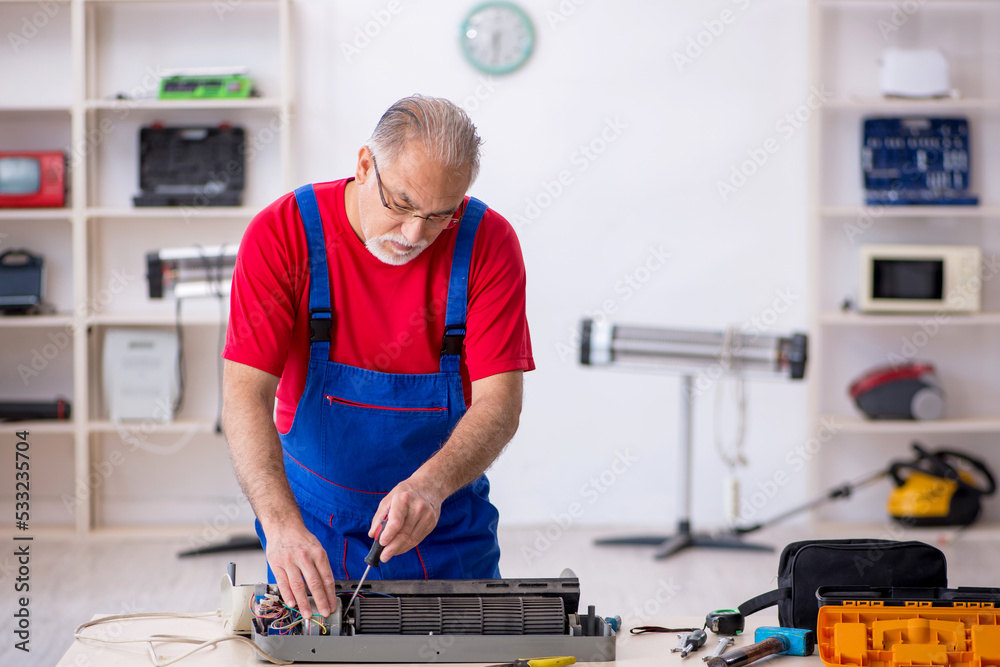Old repairman repairing air-conditioner at workshop Old repairman repairing air-conditioner at workshop
