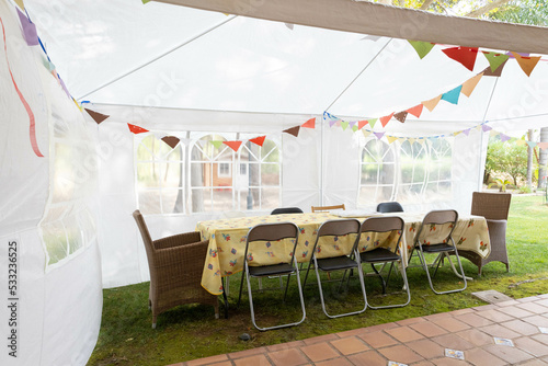 Tent ready for a birthday party with the family, with some colourful flags, and a table with some  different chairs