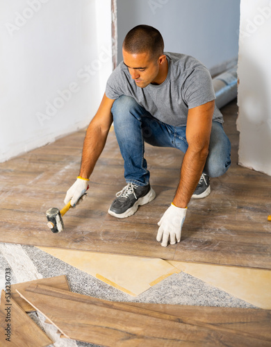 Man using hammer to lay down wooden parquet on floor. Renovation works in new apartment.