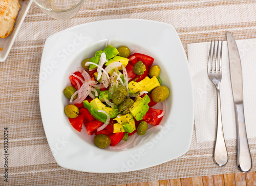 Fresh vegetable salad on white plate. Salad include avocado, tomatoes, olives, onion and condiment.
