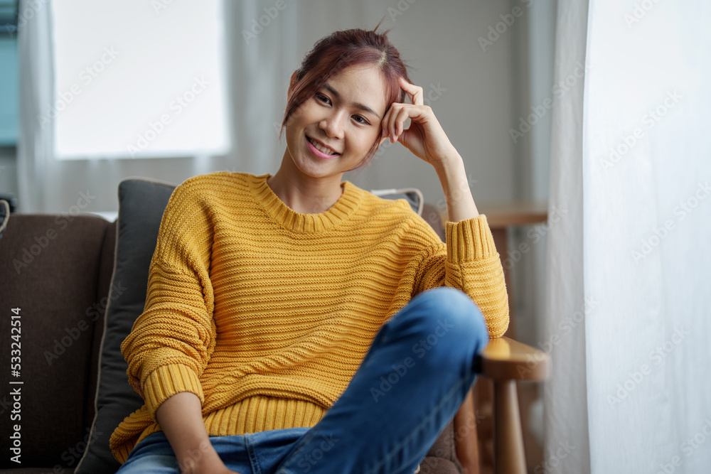 A portrait of a young Asian woman resting with a smiling face on the sofa by the window of the house A portrait of a young Asian woman resting with a smiling face on the sofa by the window of the house