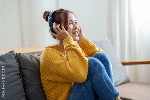 portrait of a young Asian woman woman using headphones holding smartphone while sitting on sofa