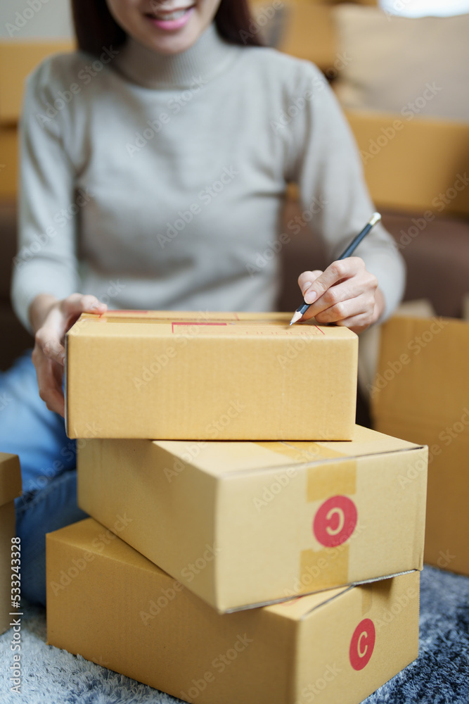 A portrait of a small startup, and SME owner, an Asian female entrepreneur, is writing down information on a box to organize the product before packing it into the inner boxes for the customer A portrait of a small startup, and SME owner, an Asian female entrepreneur, is writing down information on a box to organize the product before packing it into the inner boxes for the customer