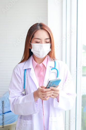 Asian female doctor working in office Wearing a mask, holding a smartphone, making online video calls, talking to patients remotely. online medical concept Hospital medical services