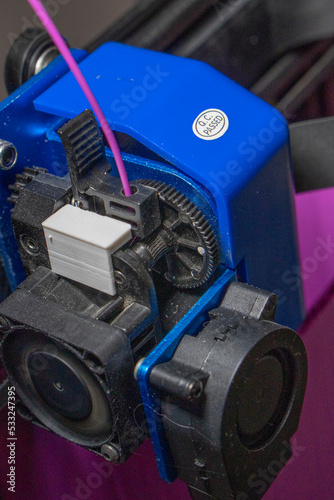 extrusor de una impresora 3d con filamento de color purpura o morado. Se ven los engranajes