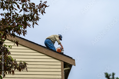 Senior man with a leaf blower on the roof of a residential home blowing debris out of gutters and off roof, fall maintenance  © knelson20