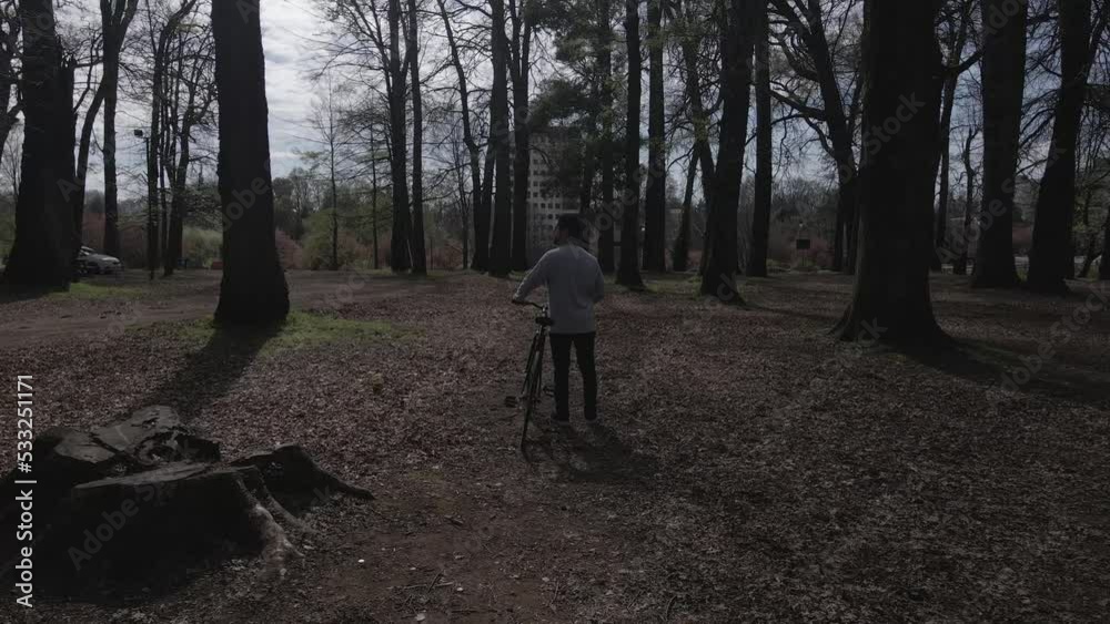 Man walking in a park with his bike stops to look at something Man walking in a park with his bike stops to look at something