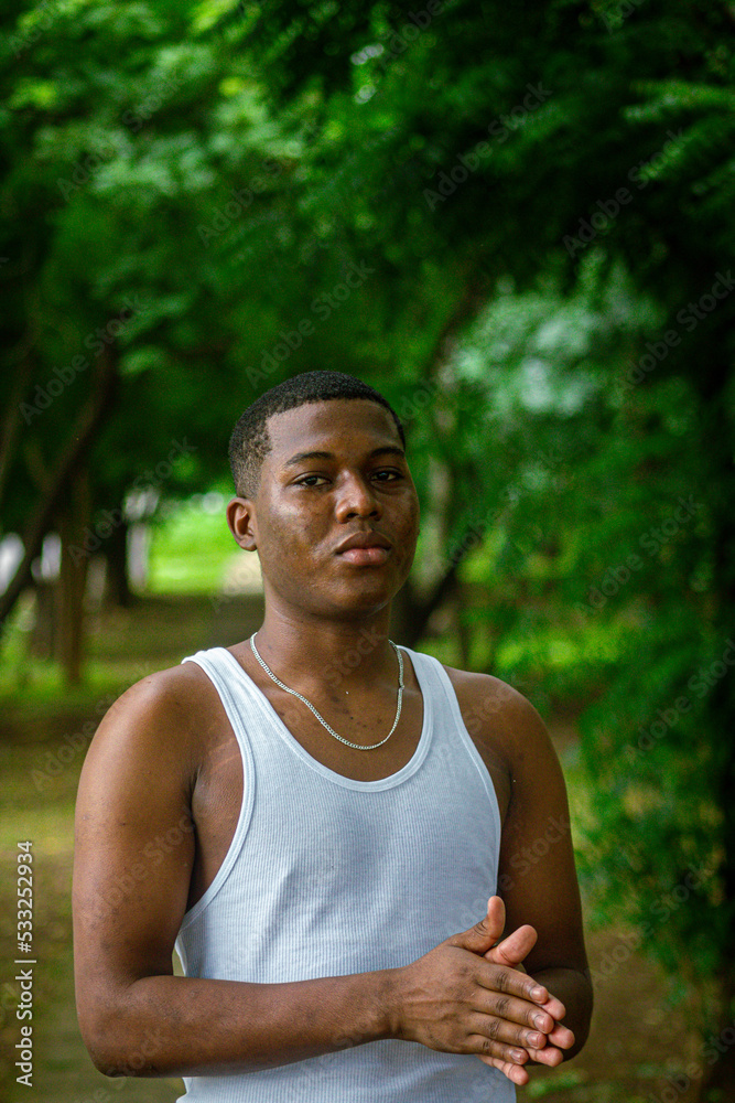 Chico afro latino viendo al frente usando una camiseta blanca con fondo verde y boscoso Chico afro latino viendo al frente usando una camiseta blanca con fondo verde y boscoso