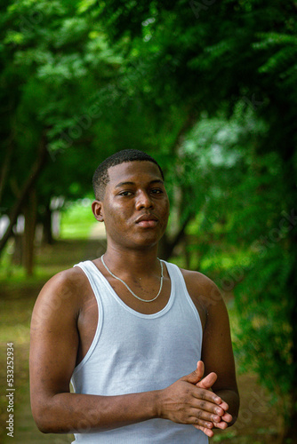 Chico afro latino viendo al frente usando una camiseta blanca con fondo verde y boscoso