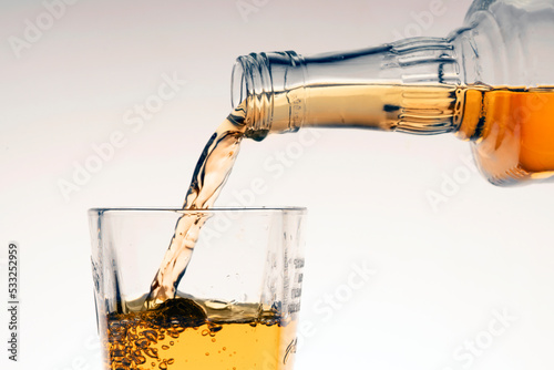 pour whiskey or bourbon into a glass on a beige white background