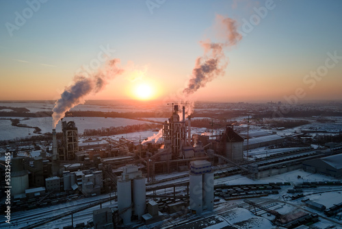 Aerial view of cement factory with high concrete plant structure and tower crane at industrial production area in evening. Manufacture and global industry concept