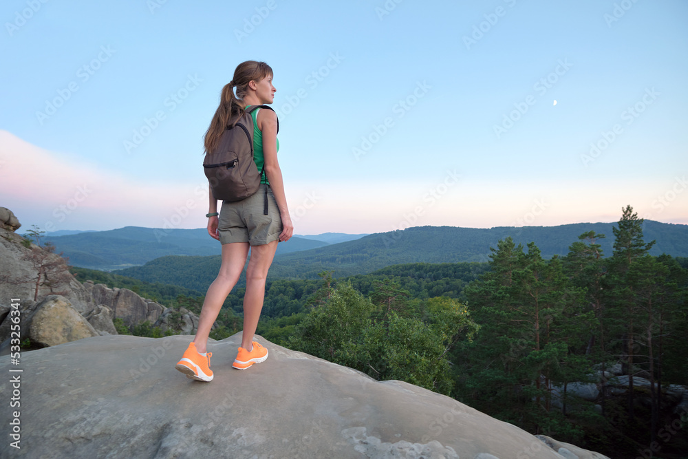 Young woman hiking alone on mountain footpath. Female hiker enjoying view of evening nature on wilderness trail. Active way of life concept