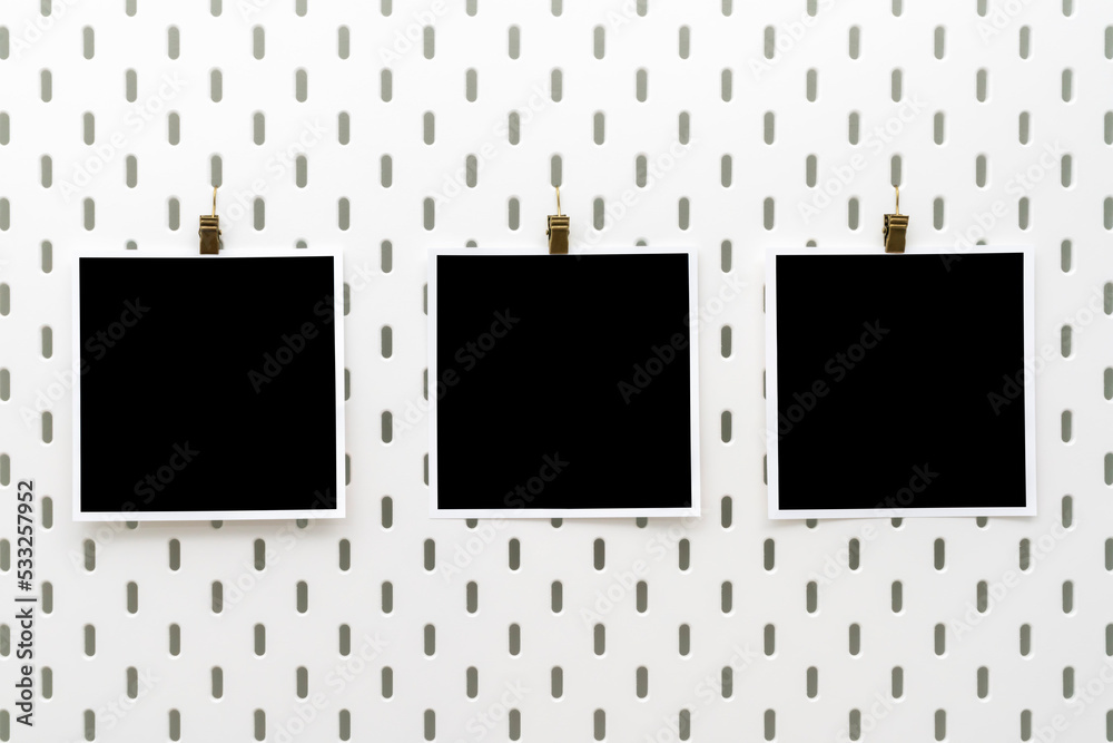 Three blank photo frames with clips on peg board. Template for