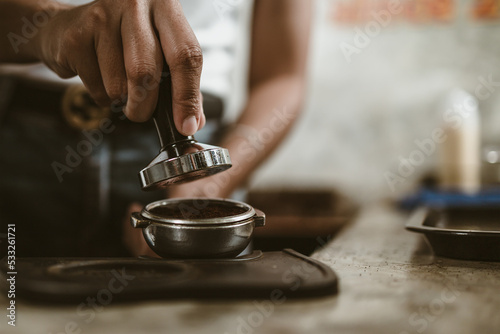 Fotografija Barista using a tamper to press ground coffee into a portafilter