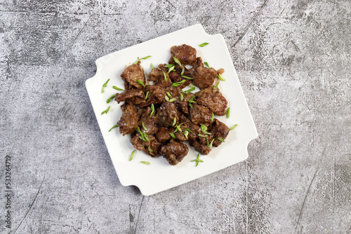 Pan fried chicken liver with herbs on a white square  plate on a dark background. Top view, flat lay