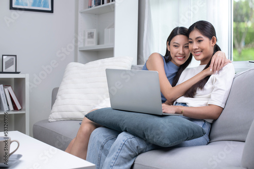 Beautigul young Asian lesbian couple communicating online on laptop. LGBT lesbian couple embracing watching movie webinar on laptop studying e-learning together, doing paperwork, paying bills online.
