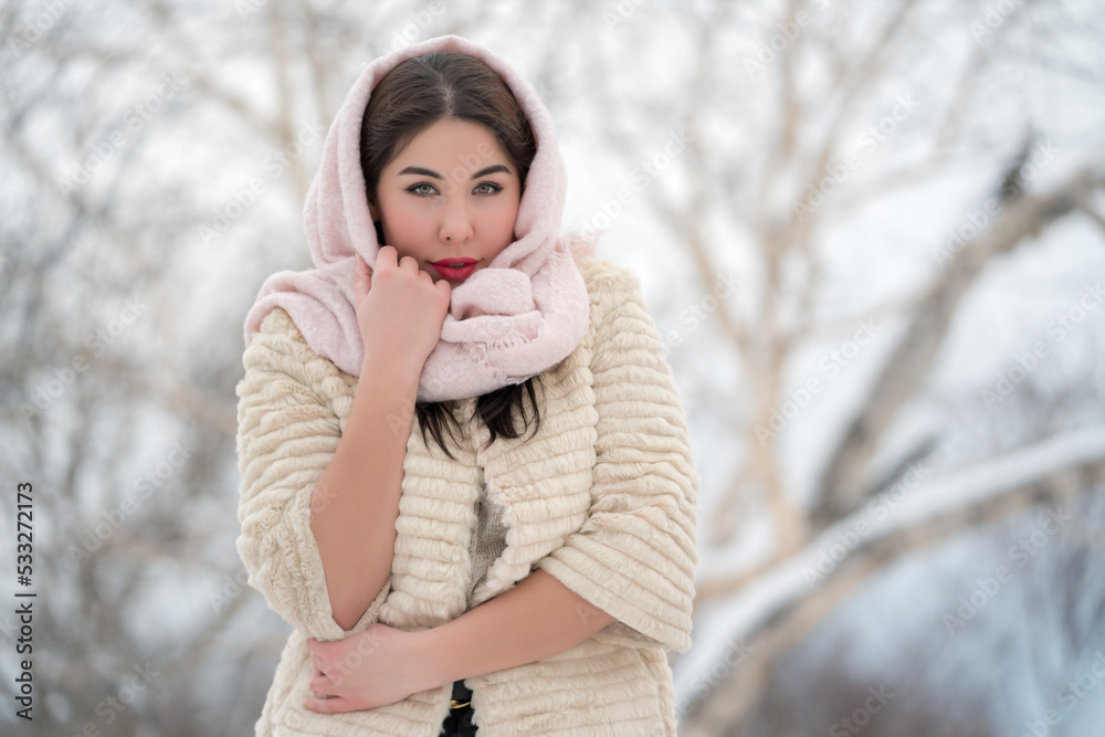 Authentic brunette young woman dressed in white three-quarter sleeve fur coat and light pink scarf on head looking at camera on winter day outdoors. Shallow depth of field, selective focus foreground Authentic brunette young woman dressed in white three-quarter sleeve fur coat and light pink scarf on head looking at camera on winter day outdoors. Shallow depth of field, selective focus foreground