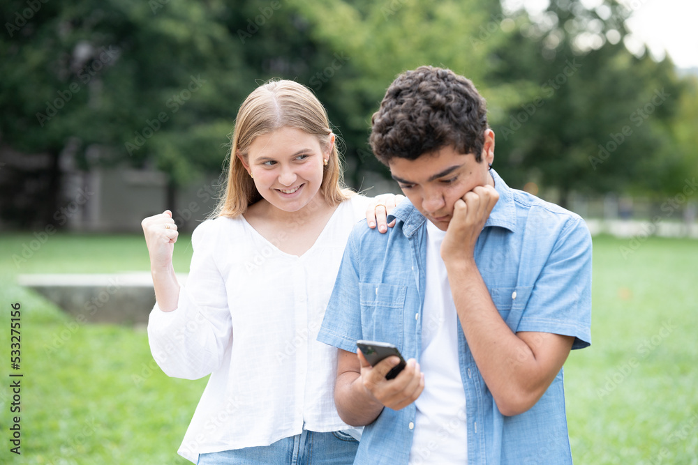Hypocrite girl celebrating friend's worry. Boy receiving bad news on phone. Hypocrite girl celebrating friend's worry. Boy receiving bad news on phone.