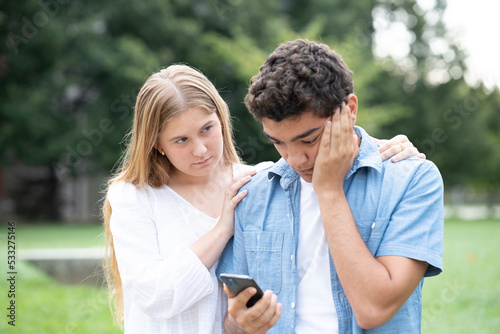 Hispanic teenager boy receiving bad news on phone and girl comforting him.