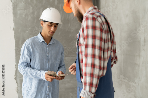 Young Businessman giving a money to builder for the work standing at the construction site. Engineering Manager pay salary or wage to worker after finishing work. photo