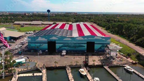 Drone view flying away from Legendary Marine in Destin Florida with the roof painted as an American Flag and it says God Bless America. You can also see the midbay bridge and Lulu's restaurant.