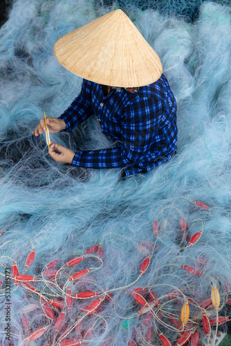 A fishing net with Vietnamese woman doing repairs sitting in traditional clothes and hat repairing a using a nylon thread. This net is used for catching shrimp.