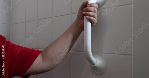 Adult female hands holding on to a safety bar next to the toilet in the bathroom, woman with motor disability problems. Concept of objects to facilitate the daily life of people with disabilities