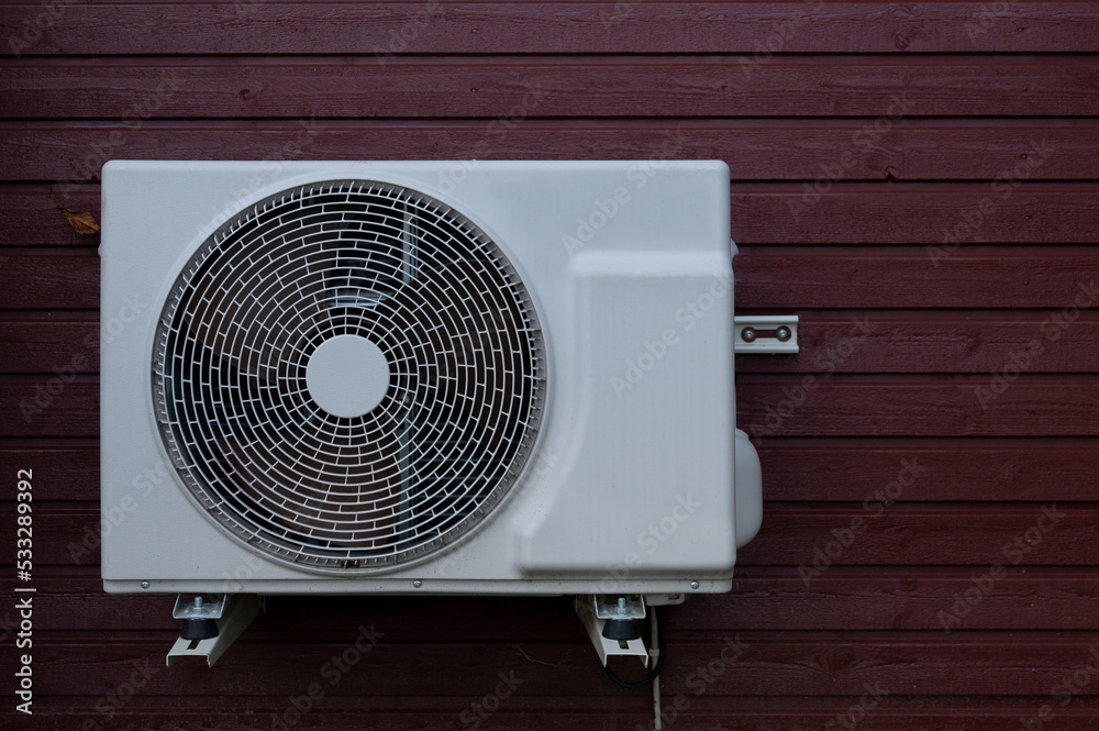 a white heat pump unit mounted on a red wood panel