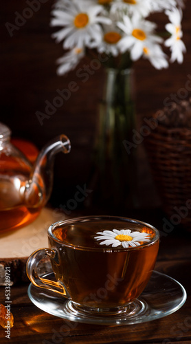 A teapot and a mug of tea on a wooden table and a bouquet of daisies