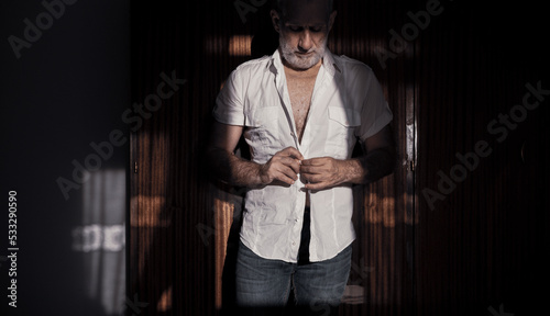 Adult man putting on shirt in bedroom