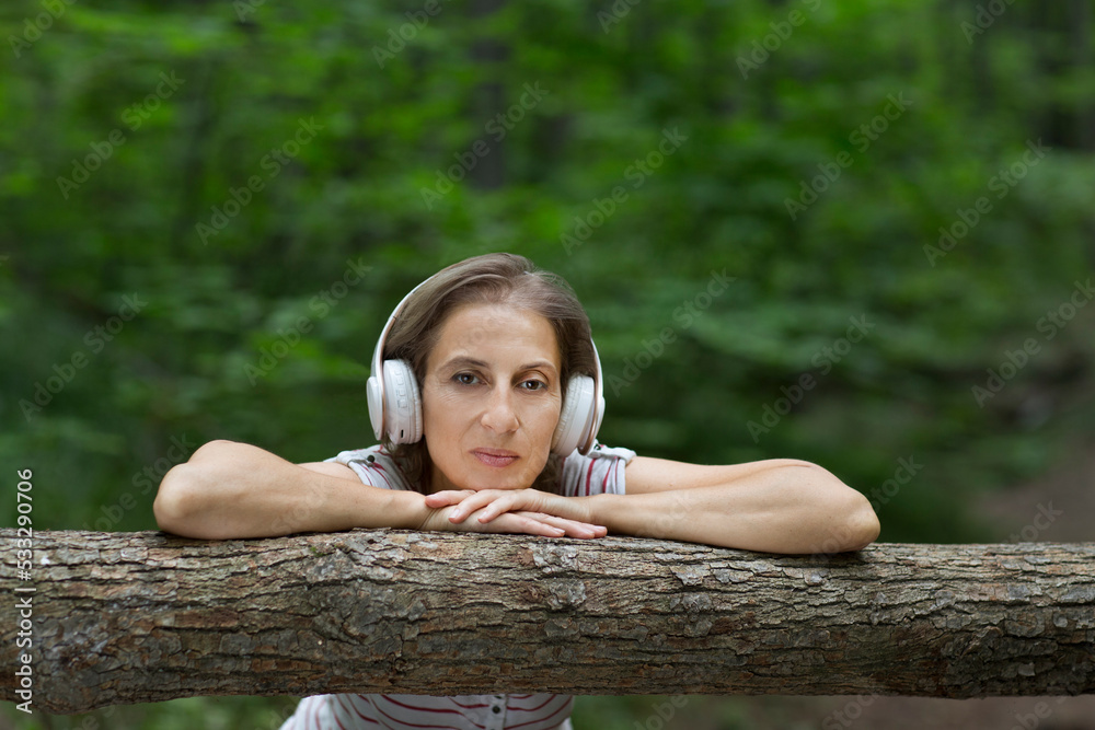 Audio healing. meditation. middle aged woman wearing headphones listens to music in the forest. Lykke concept,
