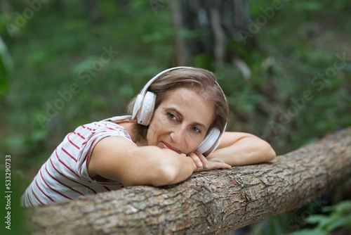 Audio healing. meditation. middle aged woman wearing headphones listens to music in the forest. Lykke concept, 