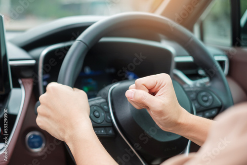 woman driver honking a car during driving on traffic road, hand controlling steering wheel in vehicle. Journey, trip and safety Transportation concepts © Jo Panuwat D