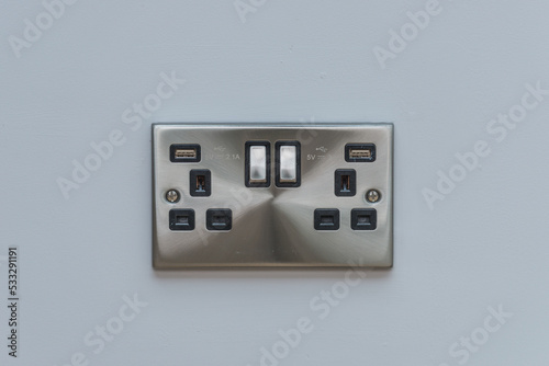 UK brushed brushed stainless steel double socket, with usb charging points, on grey wall.