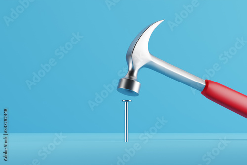 Photography Claw hammer with red plastic handle hitting a nail on blue background