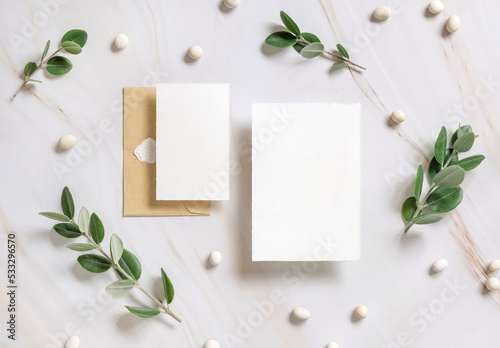 Cards and envelope on a marble table near eucalyptus branches and pebbles top view, Wedding mockup