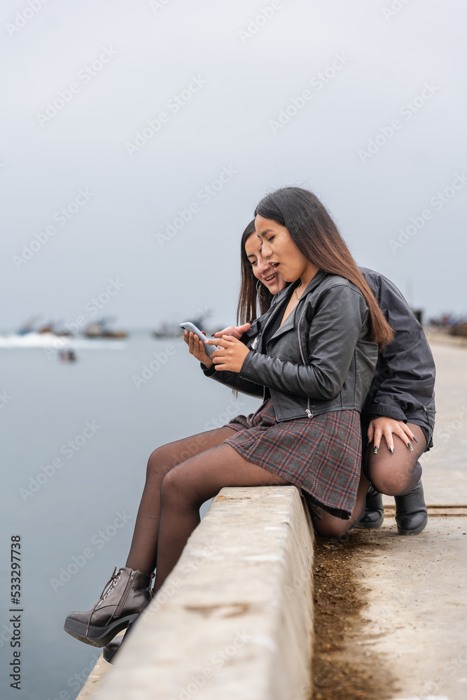 Friends with a surprised look while using a mobile sitting facing the sea