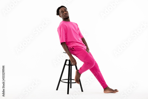 Handsome african american man posing leaning back on chair looking at camera seriously showing angry thoughtful emotions wearing stylish pink costume.