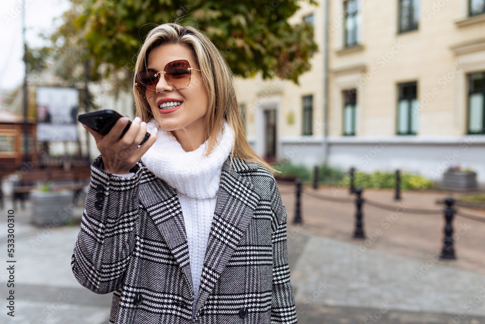 stylish woman entrepreneur adult speaks on the speakerphone of a mobile phone in the city